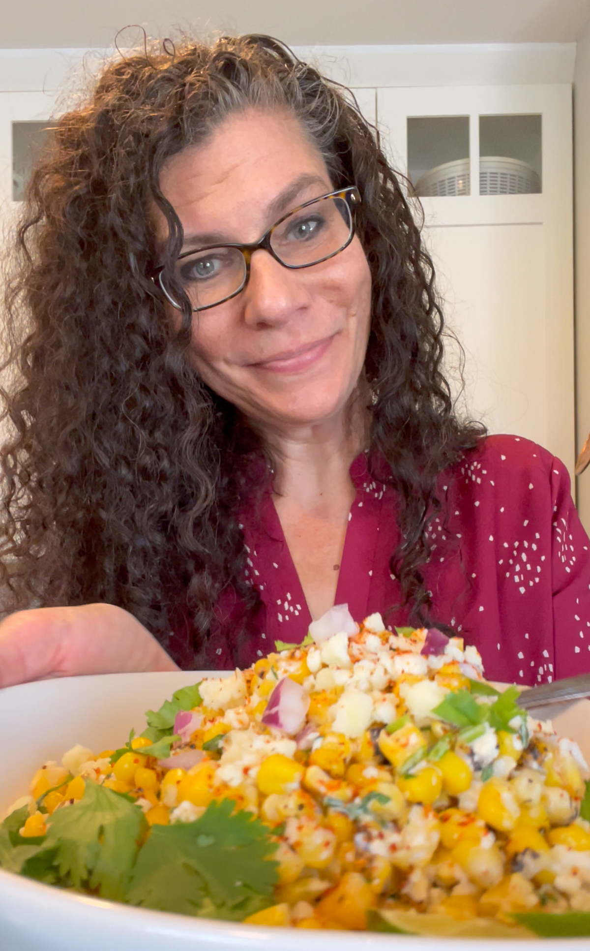 Jenni standing in front of white kitchen cabinets holding a white bowl with salad